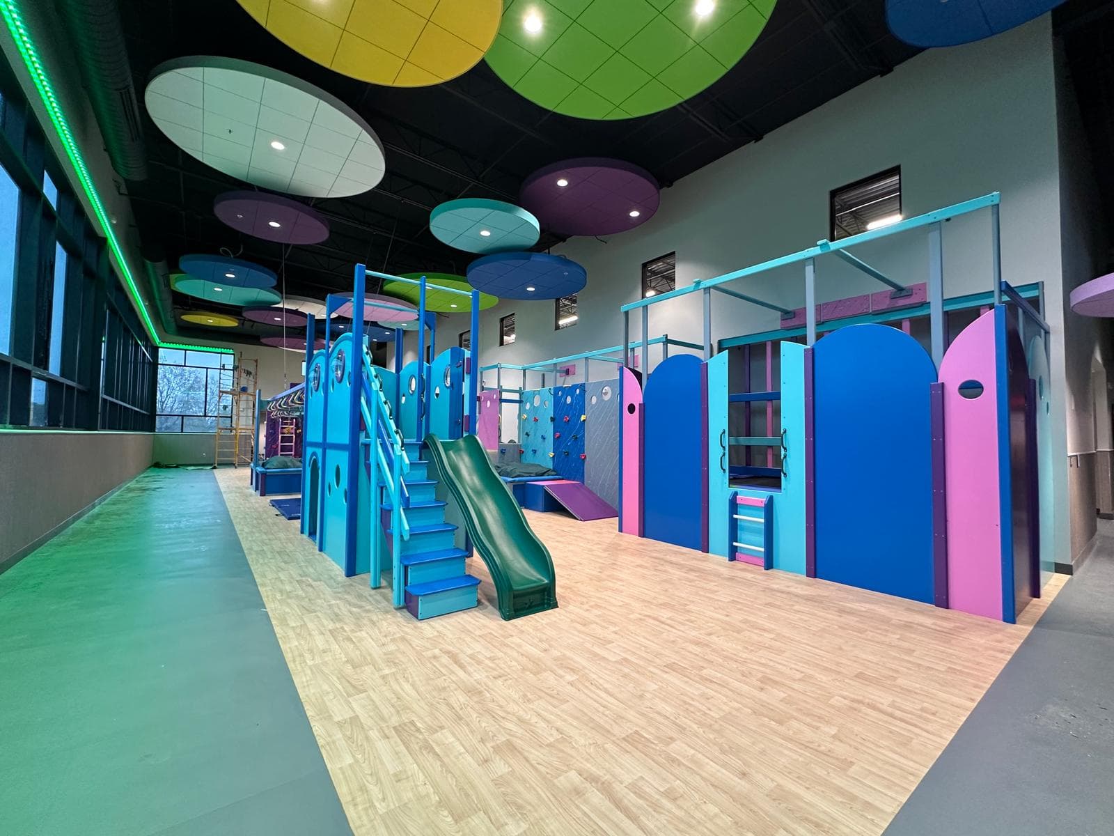 Large commercial sensory gym with colorful ceiling discs, multiple climbing stations, and slides